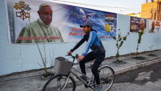 In this Feb. 27, 2021, file photo, a boy cycles past a poster welcoming Pope Francis, who is expected visit Iraq in March, hanging on the wall of the Chaldean Catholic Church of St. Joseph in the capital Baghdad.