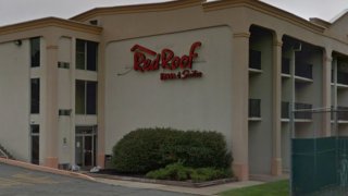 A wall reads "Red Roof inn & suites." Balconies can be seen on each side of the wall, as can a hedge in front of it.