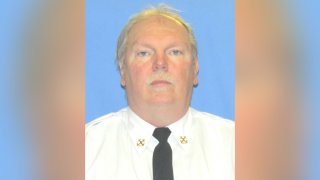 John Evans, a Philadelphia firefighter who died of COVID-19, wears a white button-up shirt and black tie as he stares ahead in a portrait photo.