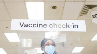 A worker stands behind a plastic protective barrier to check-in people recieving the Moderna Covid-19 vaccine at a CVS Pharmacy location in Eastchester, New York, U.S., on Friday, Feb. 12, 2021.