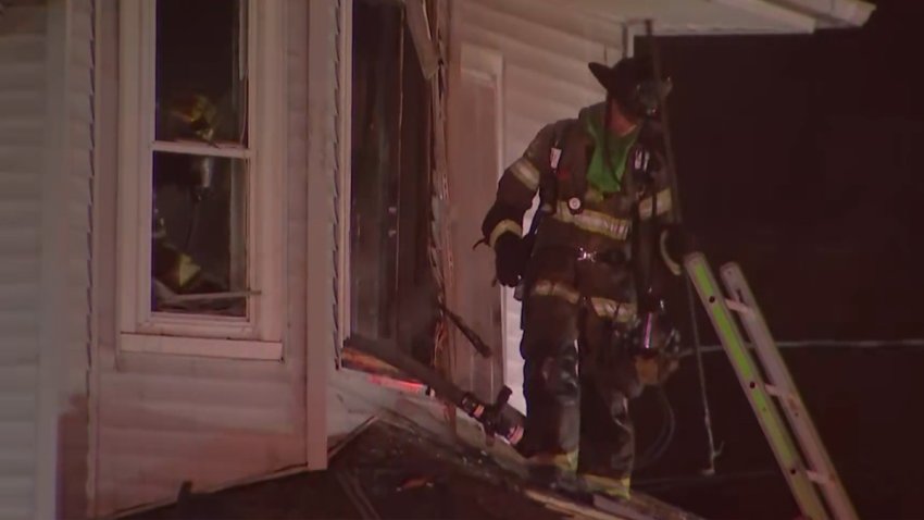 A firefighter stands on a roof, in front of a ladder, and looks down after a fire at a South Jersey home.