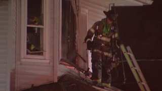 A firefighter stands on a roof, in front of a ladder, and looks down after a fire at a South Jersey home.