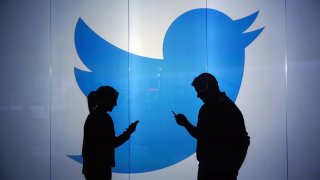 People are seen as silhouettes against an illuminated wall bearing Twitter logo