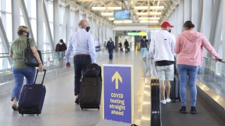 In this March 26, 2021, file photo, travelers wearing protective masks walk past a sign pointing towards a Covid-19 testing location in Terminal 5 at John F. Kennedy International Airport (JFK) in New York.
