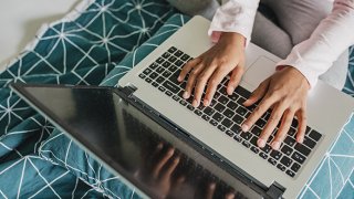 Top view of child's hands using laptop at home in bed