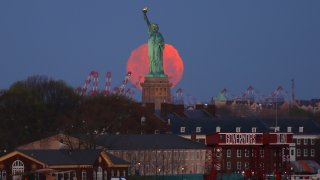 An almost full Pink Moon is seen in the sky behind the Statue of Liberty as the sun rises on April 26, 2021, in New York City. The Super Pink Moon will rise later in the day.