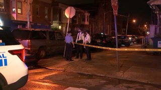 Philadelphia police officers stand at a West Philadelphia street corner near where a man was gunned down.