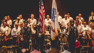 An orchestra with three servicemembers holding flags