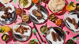 Food is laid out on a table. It includes chops, falafel and sauces and dips.