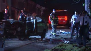 Police and rescuers stand around two vehicles involved in a crash. One vehicle's front end is caved in, while the second is damaged by a utility pole.