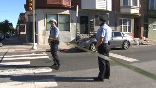 Two Philadelphia police officer stand behind crime scene tape as they block off a street where a 16-year-old boy was shot.