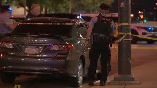 Police look on at a car parked on the side of the street behind crime scene tape after a shooting at an Insomnia Cookies store on Temple University's campus.