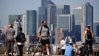 Pedestrians relax in the sunshine in Greenwich Park in view of skyscrapers in the Canary Wharf business, shopping and financial district in London, U.K., on Monday, March 29, 2021.