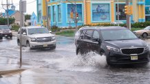 This Oct. 11, 2019 photo shows cars kicking up spray while driving through a flooded intersection at the entrance to Long Beach Island in Ship Bottom, N.J. With the highest tides of the year expected to arrive in New Jersey during the week of May 24, 2021, the state is launching a campaign to have residents document tidal flooding in their neighborhood and upload photos to a web site.