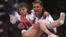 USA's Kerri Strug is carried by her coach, Bela Karolyi, as she waves to the crowd on her way to receiving her gold medal for the women's team gymnastics competition, at the Centennial Summer Olympic Games in Atlanta on Tuesday, July 23, 1996. Strug suffered two torn ligaments and a sprained ankle from the vault competition.