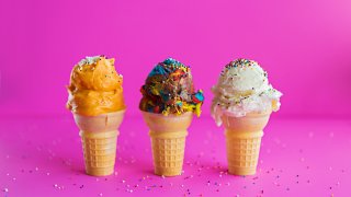 Three varied flavored, ice cream, single scoop, cones with sprinkles in a row on a bright pink background.