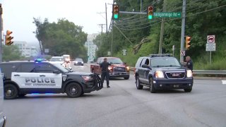 Police officers and patrol SUVs block off a road and divert cars.