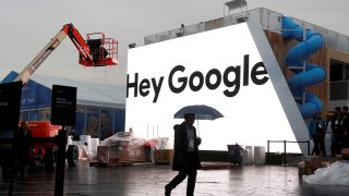 A man walks through light rain in front of the Hey Google booth under construction at the Las Vegas Convention Center in preparation for the 2018 CES in Las Vegas, Nevada, January 8, 2018.