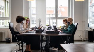 Employees working at their desks with screen partition in between them, back to work after Covid-19 pandemic.