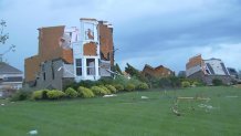 A multi-story home can be seen with its roof collapsed and blown out windows in front of a green lawn after a tornado ripped through the area.