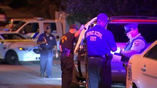 Detectives stand around an SUV, one flashing a light and looking inside, after a deadly shooting in West Philadelphia.