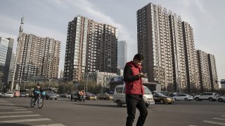 A pedestrian crosses a road in front of residential buildings in Beijing, China.