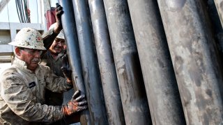 Workers guide a section of drill pipe into a rack after it was removed from a natural gas well being drilled in the Eagle Ford shale in Karnes County, Texas.