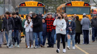 Parents walk away with their kids from the Meijer's parking lot where many students gathered following an active shooter situation at Oxford High School in Oxford, Michigan, Nov. 30, 2021.