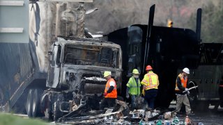 FILE – Workers clear debris from the eastbound lanes of Interstate 70 on April 26, 2019, in Lakewood, Colo., following a deadly pileup involving a semi-truck hauling lumber.