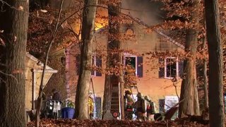 Flames shoot up from a house as a firefighter climes a ladder to try to enter through a second-story window.