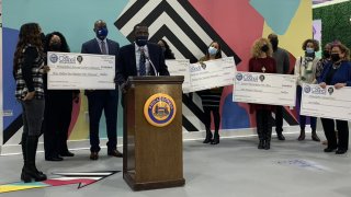 Philadelphia City Councilman Isaiah Thomas stands in front of a podium as people behind him hold large checks.