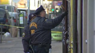 A Philadelphia crime scene officer wears a jacket and hat as he knocks on a door. His partner stands next to him.