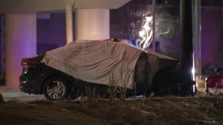 A white sheet is draped over a sedan with fire damage.