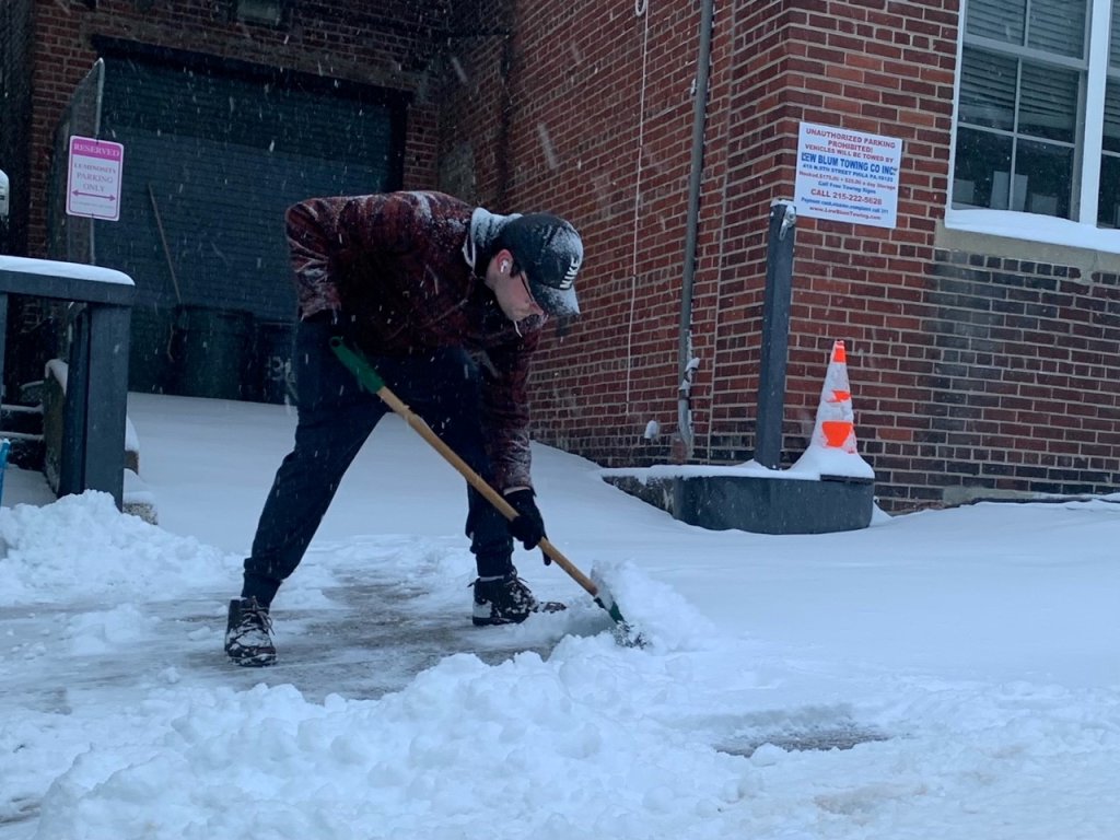 A man crouches down to shovel snow on Levering Street in Philadelphia's Manayunk neighborhood.