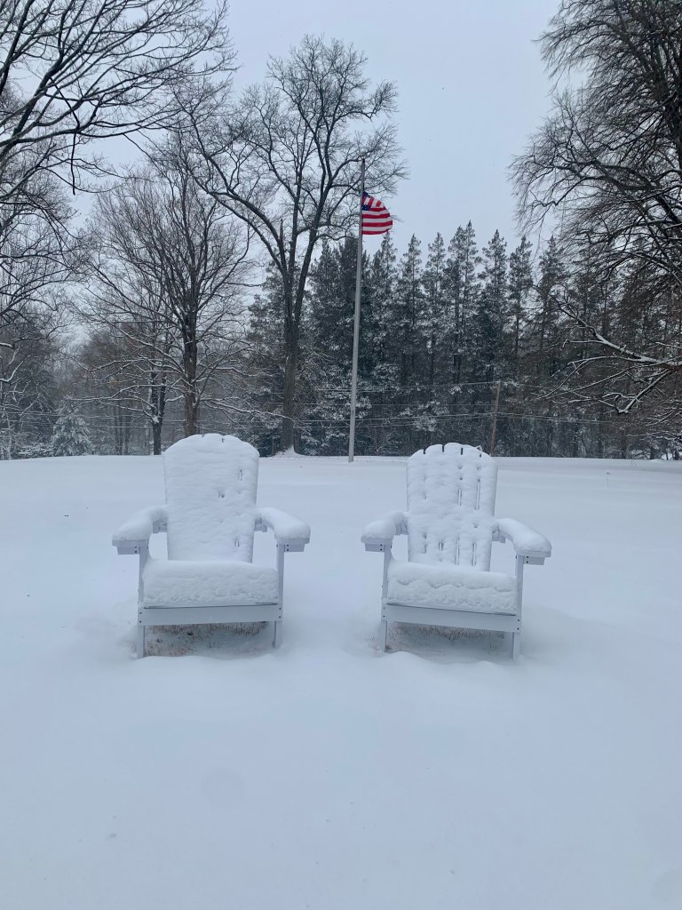 Snow-covered lawn chairs as an American flag on a pole waves behind.