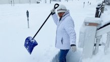 A person in a jacket and beanie holds a shovel as snow covers the street in Ocean City, New Jersey.