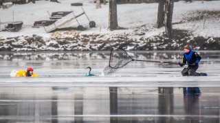 This photo provided by Michelle Handley, Lt. Luke Boucher from the Monmouth Fire Department, left, swims to a loon while Bill Hanson of the Biodiversity Research Institute holds a net during a successful effort to rescue the bird that was trapped on Sand Pond in the Tacoma Lakes Sunday, Jan. 2, 2022 in Monmonth, Maine.