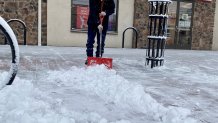 A man in a hoodie and wearing a face mask shovels snow from in front of a building in Delaware.