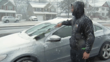 A man wearing a hoodie wipes snow off the windshield of his car in North Wales, Pennsylvania.