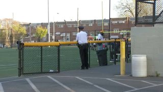 A police officer leans on a fence surrounding a youth football field.