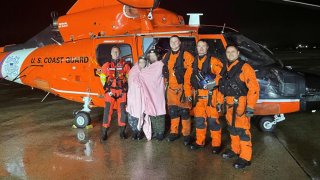 Coast Guard members pose with a couple wrapped in a blanket in front of a helicopter