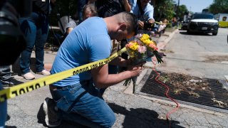 Joseph Avila, left, prays while holding flowers honoring the victims killed in Tuesday's shooting at Robb Elementary School in Uvalde, Texas, Wednesday, May 25, 2022.