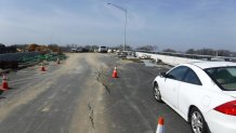 A car is parked on a cracked piece of road that has cones on top of it.