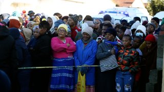 People stand behind a police cordon outside a nightclub in East London, South Africa, Sunday June 26, 2022.