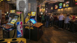 Arcade games and a bar with people sitting and enjoying drinks.