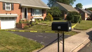 A mailbox has police crime scene tape tied to it. Behind the mailbox is a home.