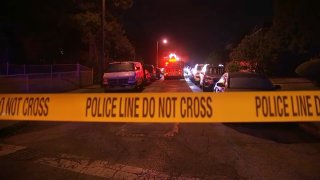 Police crime scene tape in the foreground. Background shows fire truck with sirens on parked in the middle of the street and flanked by cars.