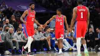 Koel Embiid slaps hands with Tyrese Maxey as James Harden looks on
