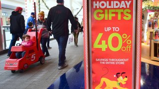 Christmas week shoppers walk past signs offering sales at a Montebello shopping mall in Montebello, California on December 22, 2016.