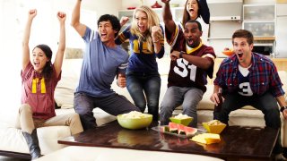 Friends cheering while watching a football game mid-day in living room.